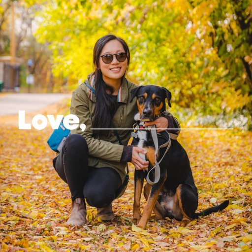 A woman with dark hair is kneeling beside a black and tan dog. The woman is wearing a green jacket, black rights, and brown boots.